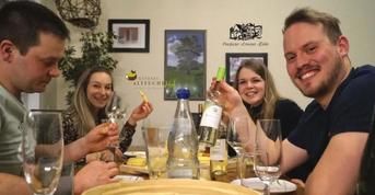 A sociable group of four people at a shared meal. They hold glasses and bottles in their hands and enjoy the moment.