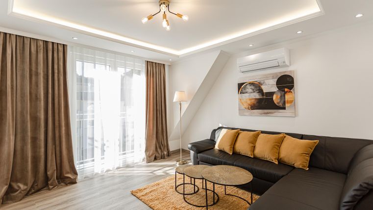 A modern living room with a comfortable black couch and decorative pillows. Large windows let in plenty of light and create a bright atmosphere.