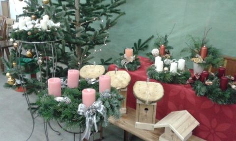 Een versierde tafel met kerstkransen, kaarsen en een kleine boom. De omgeving is feestelijk versierd en in warme kleuren gehouden.