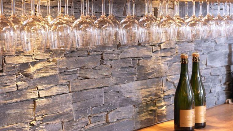 Eine elegante Bar mit einem Steinwand-Design und hängenden Weingläsern. Zwei Flaschen Sekt stehen auf der Holzoberfläche.