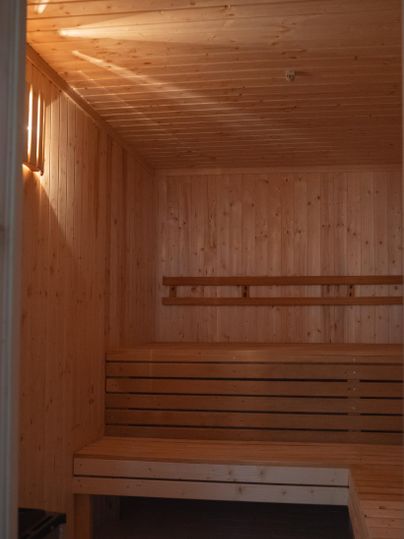 Een gezellige sauna met houten wanden en banken. Het licht straalt zachtjes van boven en creëert een ontspannende sfeer.