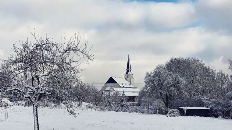 Verschneite Landschaft mit Kirche und Bäumen im Hintergrund.