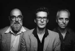 Three men pose in a portrait against a dark background. They are wearing formal attire and looking directly at the camera.