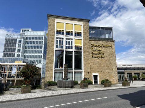 Ein modernes Gebäude mit großen Fenstern und gelben Jalousien. Im Hintergrund sind weitere moderne Gebäude zu sehen.