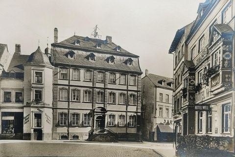 A historical street scene with several buildings in classical style. On the right side, there is a hotel marked with a sign.