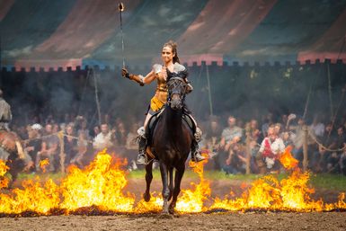 Eine Frau reitet auf einem Pferd durch Feuer bei Ritterspielen