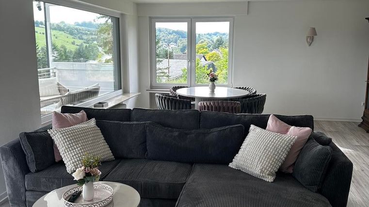 Ein modernes Wohnzimmer mit einem bequemen dunkelgrauen Sofa und einem runden Beistelltisch. Große Fenster bieten einen Blick auf die grüne Umgebung.