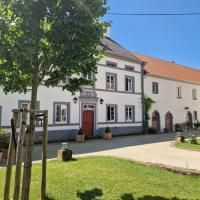 Een groot, wit huis met een rood dak. Omgeven door groene gras en bomen op een zonnige dag.