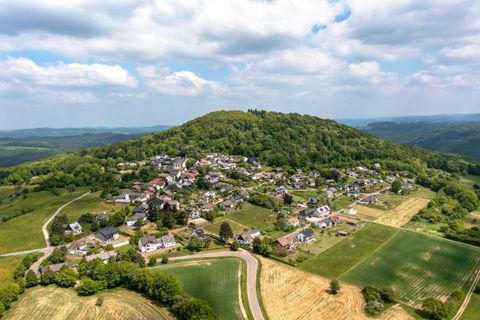 Eine Luftaufnahme eines kleinen Dorfes, umgeben von grünen Hügeln und Feldern. Der Himmel ist bewölkt, und die Landschaft ist malerisch und friedlich.