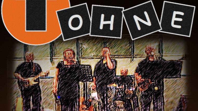 Une bande joue sur la scène, composée de plusieurs musiciens. En arrière-plan, il y a un grand logo orange avec une flèche.