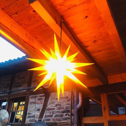 Eine leuchtende Sternenlampe hängt unter einer Holzdecke. Das warme Licht strahlt eine gemütliche Atmosphäre aus.