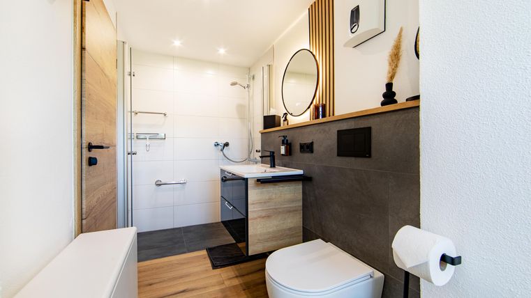 A modern bathroom with neutral colors and wooden details. It features a large mirror and an elegant shower.