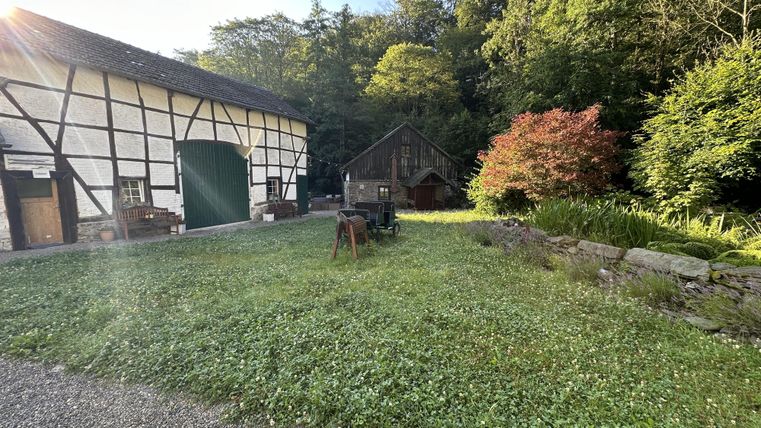 Une ferme idyllique avec une vieille maison à colombages et une grange confortable. Le jardin verdoyant est entouré d'arbres et de fleurs.