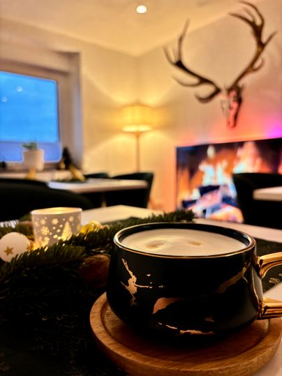 A cozy interior view with a coffee in an elegant cup. In the background, a fireplace flickers and a deer antler adorns the wall.
