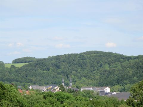 Eine malerische Landschaft mit sanften Hügeln und üppigem Grün. Im Vordergrund sind kleine Häuser und Kirchtürme sichtbar.