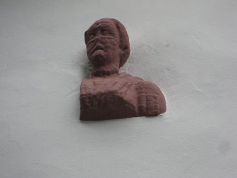 A torso of a man emerges from a white wall.
The statue made of reddish stone consists of a head and chest and dates back to the Roman era.