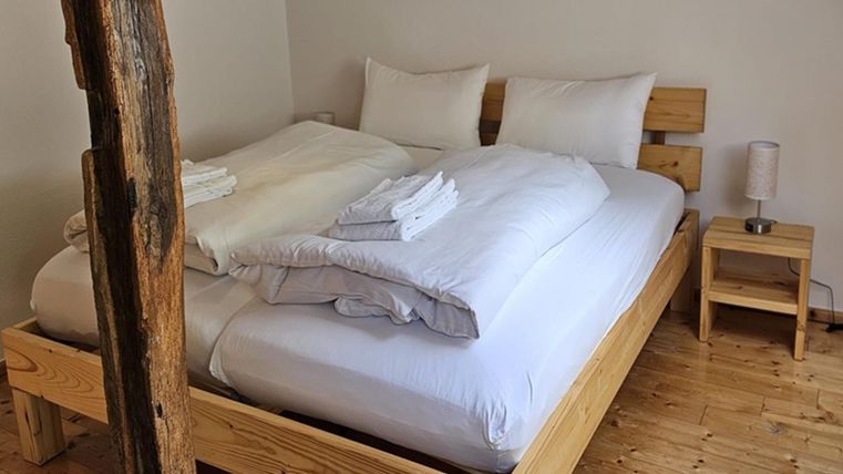 Een gezellige slaapkamer met een houten bed en vrolijk wit beddengoed. Naast het bed staat een klein nachtkastje met een lamp.