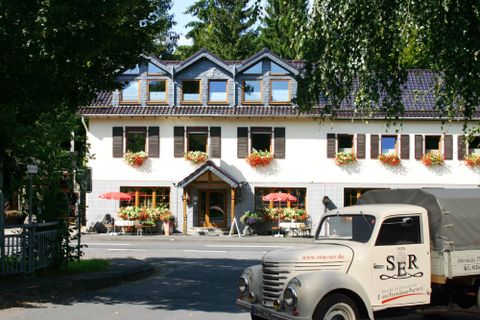 Ein charmantes Restaurant mit blühenden Blumenkästen und einer einladenden Terrasse. Im Vordergrund steht ein nostalgisches Fahrzeug, das zur Atmosphäre beiträgt.