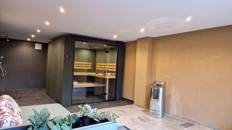 Une chambre moderne et minimaliste avec une douche en verre et des étagères en bois. Les murs sont peints dans des couleurs douces et il y a quelques plantes pour la décoration.