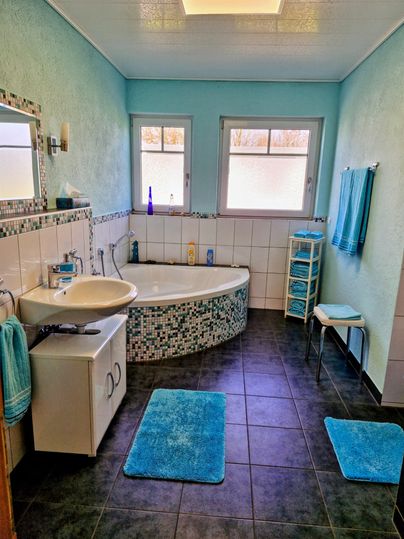 Een modern badkamer met blauwe muren en een ronde badkuip. Er zijn witte tegels, handdoeken en een kleine plank.